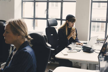 Geschäftsfrau beim Essen und Arbeiten am Laptop im Büro - MASF23152