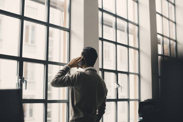 Rear view of businessman talking on mobile phone in office - MASF23157