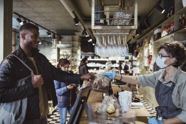 Smiling male customer collecting order from female store owner from deli store during COVID-19 - MASF23210