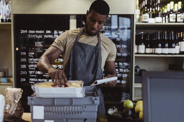 Male owner arranging order in box container at deli shop - MASF23226