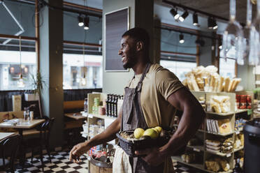 Junger männlicher Besitzer steht mit einem Obstkorb in einem Feinkostladen - MASF23227