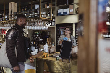 Male customer collecting order from female owner at deli store - MASF23228