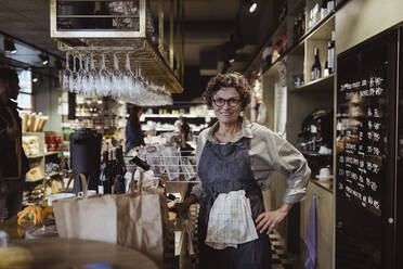 Portrait of smiling female owner with hand on hip at deli store - MASF23232