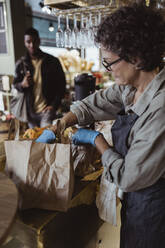 Female entrepreneur packing order in paper bag at delicatessen shop - MASF23233