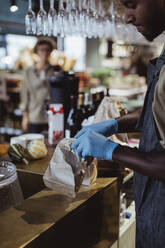 Male store owner packing food in paper bag at deli store - MASF23240