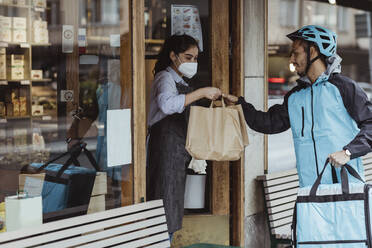 Young delivery man collecting order from female owner at delicatessen shop during COVID-19 - MASF23250