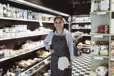 Portrait of smiling female owner with hand on hip in deli store - MASF23266