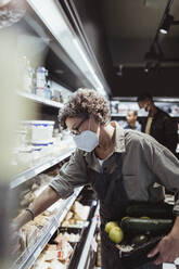 Female owner arranging food product on rack in delicatessen shop during pandemic - MASF23277