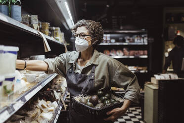 Mature male entrepreneur arranging product on rack at deli store during COVID-19 - MASF23297