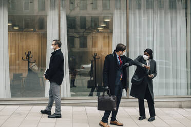 Male entrepreneur doing elbow bump with female colleague outside store during pandemic - MASF23322