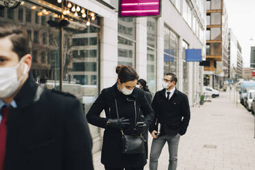 Female entrepreneur holding smart phone while standing in line with colleagues during COVID-19 - MASF23327