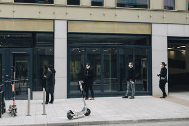 Business people standing in line on footpath by building during COVID-19 - MASF23331