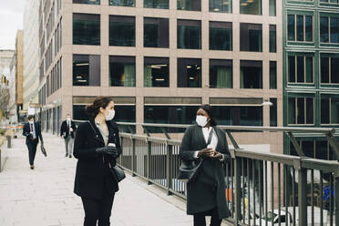 Weibliche Kollegen unterhalten sich beim Spaziergang auf einer Brücke in der Stadt - MASF23340