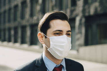 Businessman looking away against office building during pandemic - MASF23344