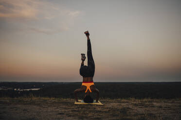 Junge Sportlerin, die bei Sonnenuntergang Yoga übt - MASF23385