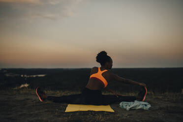 Rückansicht einer Sportlerin, die bei Sonnenuntergang Yoga macht - MASF23387