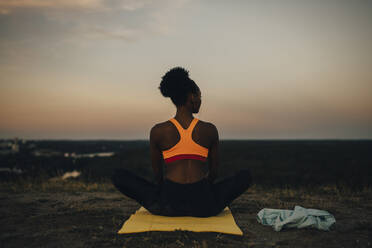 Rückansicht einer Sportlerin, die bei Sonnenuntergang auf einer Gymnastikmatte sitzt - MASF23389