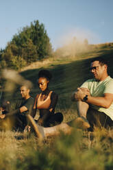 Männliche und weibliche Athleten meditieren im Gras sitzend in einem Park an einem sonnigen Tag - MASF23425