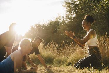 Männliche und weibliche Athleten trainieren, während ein Fitnesstrainer sie im Park anfeuert - MASF23433