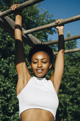 Female athlete looking down while hanging on monkey bar in park - MASF23451