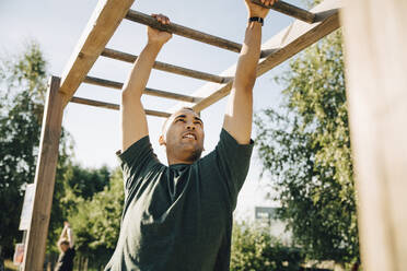 Male athlete hanging on monkey bar in park on sunny day - MASF23453