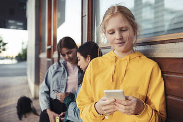 Weibliche Teenager-Freunde benutzen ihr Smartphone gegen ein Gebäude - MASF23466