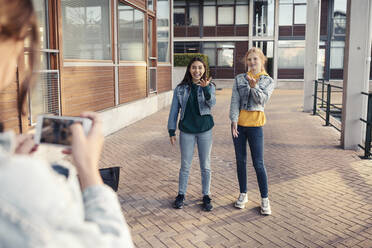 Teenage girl photographing smiling female friends on footpath against building - MASF23470