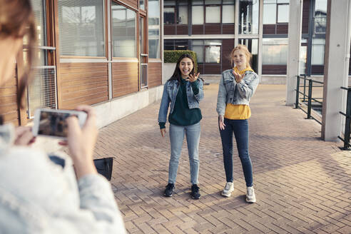 Teenagerin fotografiert lächelnde Freundinnen auf dem Fußweg vor einem Gebäude - MASF23470