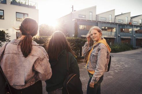 Freundinnen stehen bei Sonnenuntergang auf dem Fußweg vor einem Gebäude - MASF23480