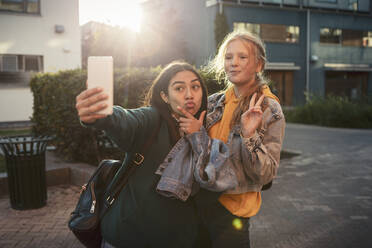 Freundinnen gestikulieren beim Selfie mit dem Smartphone auf dem Fußweg - MASF23483