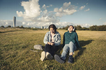 Freundinnen hören Musik über Kopfhörer, während sie ihre Freizeit im Park verbringen - MASF23496