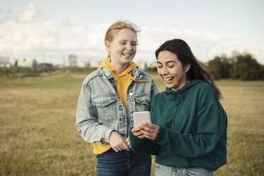 Cheerful female friends laughing while using smart phone in park - MASF23499