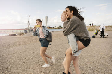 Eine Freundin nimmt sie huckepack, während ein Teenager am Strand fotografiert - MASF23511
