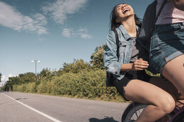 Teenage girl laughing while sitting on bicycle behind female friend on street - MASF23516