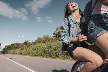 Teenager-Mädchen lachend auf dem Fahrrad sitzend hinter ihrer Freundin auf der Straße - MASF23516