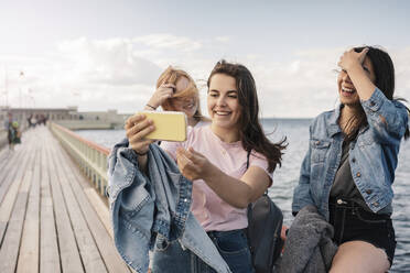 Glückliche Freundinnen nehmen Selfie durch Smartphone auf Pier gegen Meer - MASF23518