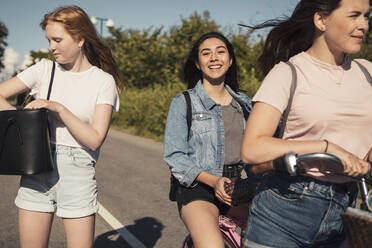 Lächelnde Freundinnen mit Fahrrad auf der Straße an einem sonnigen Tag - MASF23521