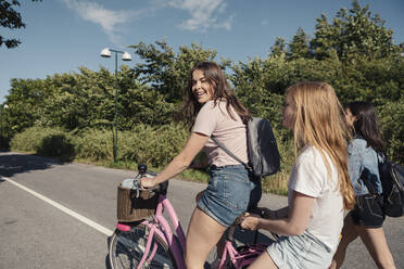 Female teenagers cycling on street during sunny day - MASF23524