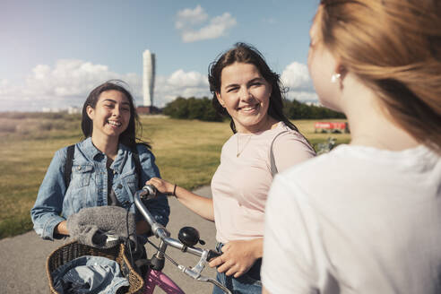 Lächelnde weibliche Teenager im Gespräch miteinander im Park während des sonnigen Tages - MASF23527