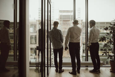 Rear view of male entrepreneurs looking through window at office - MASF23538