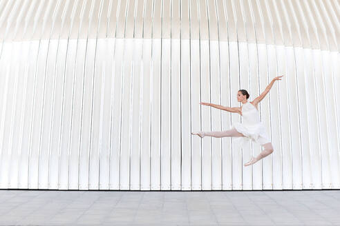Junge Balletttänzerin in Spitzenschuhen mit erhobenem Bein und Arm, die über ein gefliestes Pflaster springt - ADSF24168