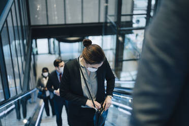 Weibliche Unternehmerin, die während der Pandemie auf der Rolltreppe in eine Umhängetasche schaut - MASF23559