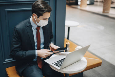 Geschäftsmann mit Smartphone und Laptop in einem Café - MASF23560