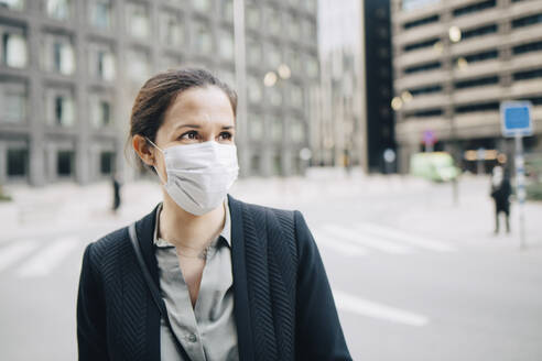 Businesswoman looking away on street in city during pandemic - MASF23585