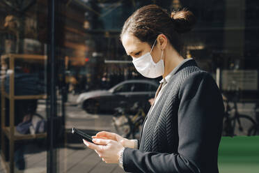 Unternehmerin benutzt Smartphone an einem sonnigen Tag während einer Pandemie - MASF23595