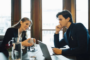 Männliche und weibliche Berufstätige, die im Büro über ihr Smartphone diskutieren - MASF23643