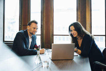 Lächelnde männliche und weibliche Kollegen, die über einen Laptop im Sitzungssaal im Büro diskutieren - MASF23652