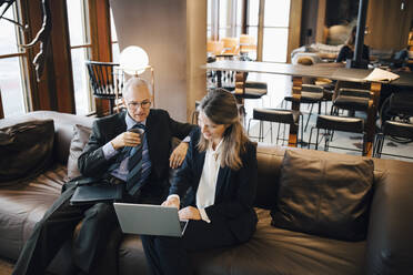 Male and female entrepreneur discussing over laptop while having coffee in cafeteria - MASF23669