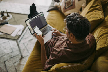 Blick von oben auf einen männlichen Unternehmer, der im Wohnzimmer an einem Laptop arbeitet - MASF23672