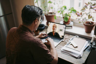 Male entrepreneur discussing with colleague on video call at home office - MASF23702